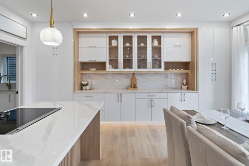 Modern kitchen featuring an island with a built-in cooktop, white shaker-style cabinetry with glass-front uppers, light wood-finish flooring, recessed lighting, and a white pendant light fixture - 13152 187 Avenue, Edmonton, AB 