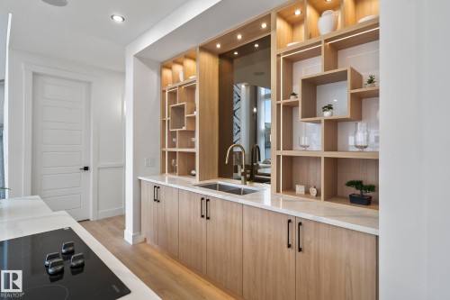Integrated wet bar featuring a single basin sink with a brass-finish faucet, under-cabinet storage, and open display shelving with integrated lighting - 13152 187 Avenue, Edmonton, AB 