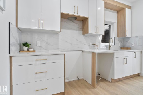 Modern kitchen featuring white cabinetry with gold-tone hardware, wood-finish accents, and a light-toned wood-finish flooring - 13152 187 Avenue, Edmonton, AB 
