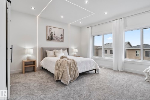 Bedroom featuring recessed ceiling lighting, integrated wall lighting, a large window array with white trim, and a barn door with a matte black handle - 13152 187 Avenue, Edmonton, AB 