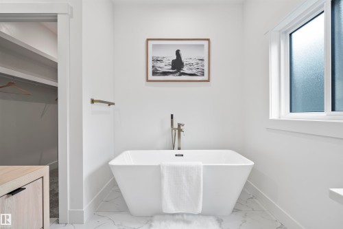 Freestanding soaking tub with floor-mounted faucet, marble-finish tile flooring, recessed lighting, and a window with frosted glass - 13152 187 Avenue, Edmonton, AB 