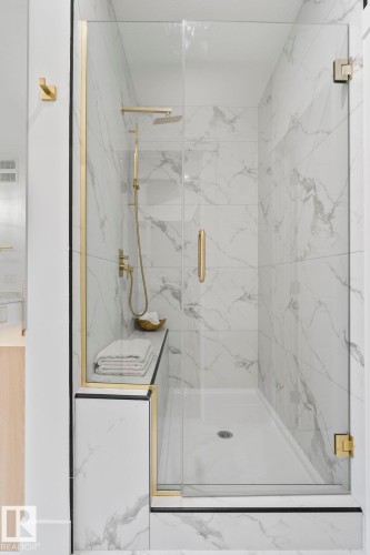 Glass-enclosed shower featuring large format veined wall tiles, a built-in shower bench, a rainfall showerhead, and gold-finish hardware throughout - 13152 187 Avenue, Edmonton, AB 