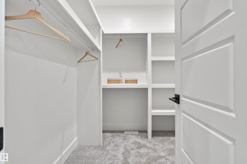 Spacious walk-in closet featuring built-in shelving, hanging rods, light gray carpet, and a white paneled door with matte black hardware - 13152 187 Avenue, Edmonton, AB 