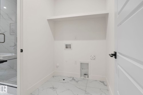 Dedicated laundry space featuring a built-in shelving unit and white tile flooring with grey veining - 13152 187 Avenue, Edmonton, AB 