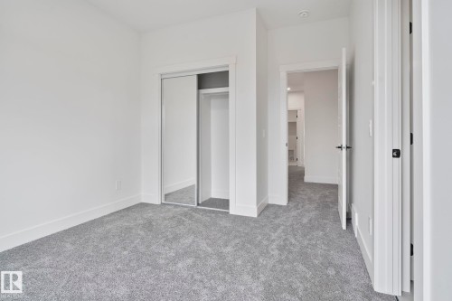 Carpeted interior room featuring a mirrored closet, white baseboards, and a neutral wall color - 13152 187 Avenue, Edmonton, AB 