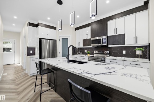 Modern kitchen featuring an expansive island with a marbled countertop and integrated sink - 8319 81 Avenue Nw, Edmonton, AB 