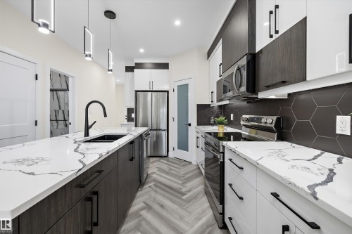 Modern kitchen featuring white and dark wood-finish cabinetry, stainless steel appliances, and a hexagonal tile backsplash - 8319 81 Avenue Nw, Edmonton, AB 