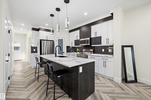 Kitchen featuring an expansive island with a waterfall countertop, integrated sink, and pendant lighting - 8319 81 Avenue Nw, Edmonton, AB 