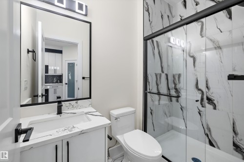 Contemporary bathroom featuring a spacious glass-enclosed shower with black-veined white tile, a white vanity with an integrated sink and black-veined white countertop, a black-framed mirror, and matte black fixtures - 8319 81 Avenue Nw, Edmonton, AB 