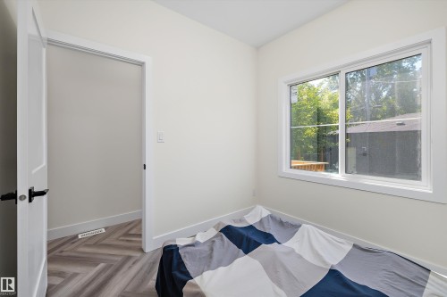 Interior room featuring a large white-framed window, neutral painted walls, and wood-finish flooring with a herringbone pattern - 8319 81 Avenue Nw, Edmonton, AB 