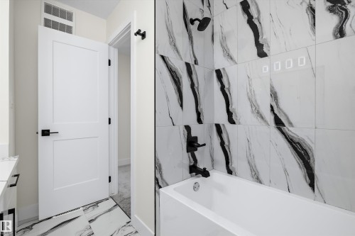 Bathroom featuring a white soaking tub with matte black fixtures, large format white and black veined wall tiles, and coordinating floor tiles - 8319 81 Avenue Nw, Edmonton, AB 