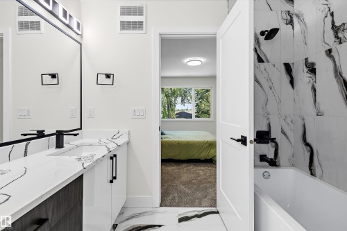 Modern bathroom featuring a single vanity with a sleek white countertop, an integrated sink, and matte black fixtures - 8319 81 Avenue Nw, Edmonton, AB 