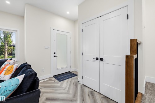 Entryway featuring wood-finish flooring in a herringbone pattern, a contemporary front door with frosted glass, and white double-panel doors - 8319 81 Avenue Nw, Edmonton, AB 