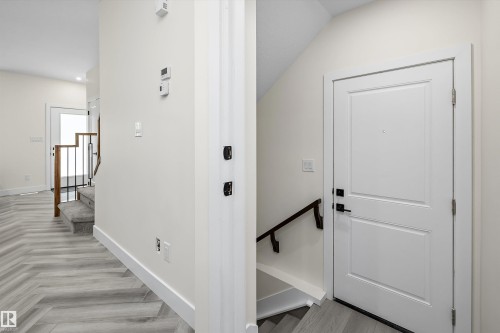 Entryway featuring a white paneled door with black hardware, light wood-finish flooring in a herringbone pattern, and a staircase with a wood handrail and black iron balusters - 8319 81 Avenue Nw, Edmonton, AB 