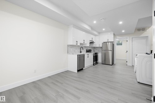 Contemporary kitchen featuring white cabinetry, stainless steel appliances, marble-look backsplash, and wood-finish flooring - 8319 81 Avenue Nw, Edmonton, AB 
