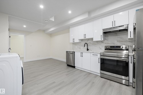 Kitchen featuring white cabinetry, stainless steel appliances, a marble-patterned backsplash, light wood-finish flooring, and recessed lighting - 8319 81 Avenue Nw, Edmonton, AB 