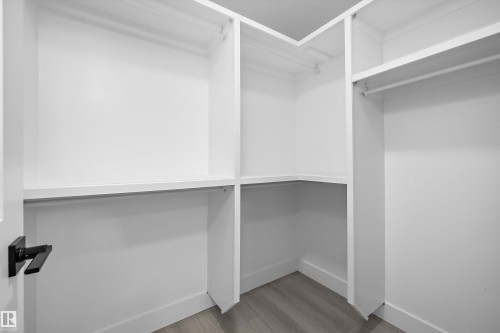 White custom closet system featuring multiple shelves and hanging rods, a corner storage section, and wood-finish flooring - 8319 81 Avenue Nw, Edmonton, AB 