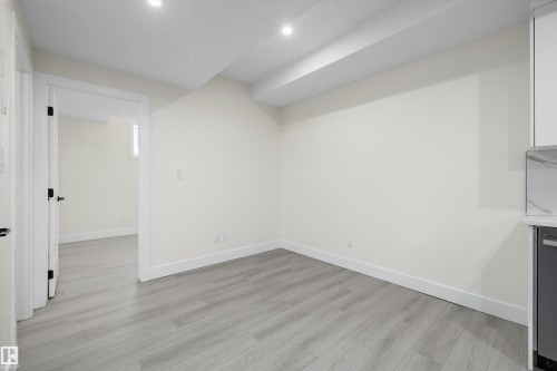 Spacious interior featuring wide plank wood-finish flooring, recessed lighting, white baseboards, and a contemporary doorway with black hardware - 8319 81 Avenue Nw, Edmonton, AB 