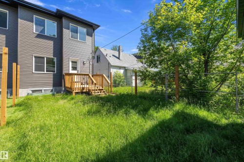 Rear exterior featuring horizontal siding, a wooden deck with stairs, multiple windows, and a wire fence - 8319 81 Avenue Nw, Edmonton, AB 