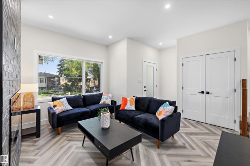 Living space featuring light wood-finish flooring in a herringbone pattern, a large picture window, recessed lighting, and a textured accent wall - 8319 81 Avenue Nw, Edmonton, AB 