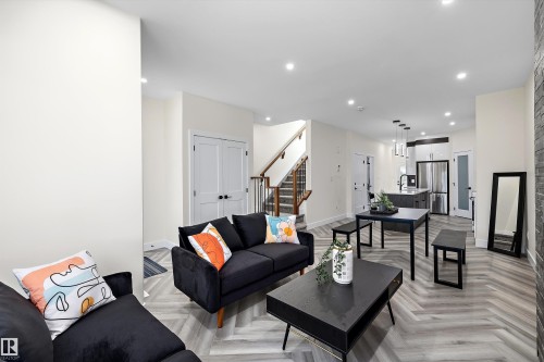 Spacious main level featuring chevron wood-finish flooring, recessed lighting, and a modern kitchen with a waterfall island - 8319 81 Avenue Nw, Edmonton, AB 