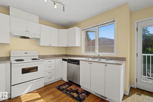 Kitchen featuring white cabinetry, a double basin stainless steel sink, and wood-finish flooring - 4259 29 Avenue, Edmonton, AB 