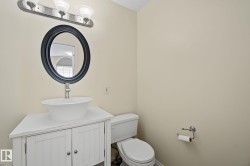 Bathroom featuring a white vessel sink on a white vanity with cabinet storage, an oval mirror with a dark frame, a three-bulb vanity light fixture, and a white toilet - 