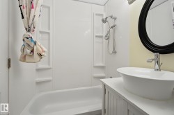 Bathroom featuring a white tub with integrated shower surround, a vessel sink with a single-handle faucet, a white vanity with cabinet storage, and an oval mirror with a dark frame - 