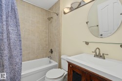 Bathroom featuring a full-size bathtub with ceramic tile surround, a built-in vanity with a white countertop, an oval wall-mounted mirror, brushed nickel fixtures, and a three-light vanity bar - 