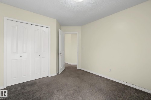 Neutral-toned room featuring a textured ceiling, dark gray carpet, and a white bi-fold closet with panel details - 4259 29 Avenue, Edmonton, AB 