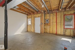 Unfinished basement space featuring exposed ceiling joists, concrete flooring, perimeter insulation, and a white access door - 