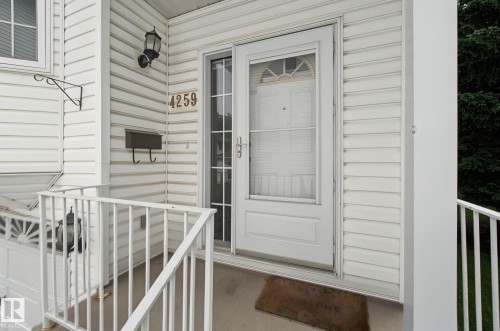 White vinyl siding exterior featuring an entryway with a storm door, an outdoor wall lantern, a wall-mounted mailbox, and white porch railings - 4259 29 Avenue, Edmonton, AB 