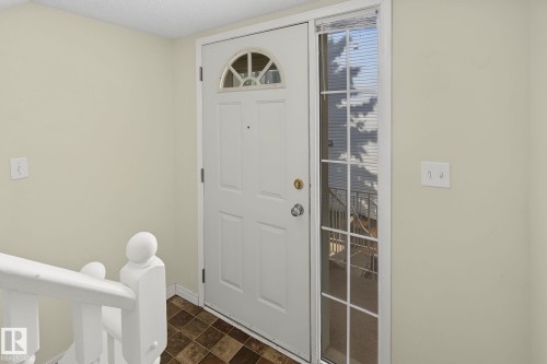 Entryway featuring a paneled door with an arched window, a full-length side window, a white painted railing, and patterned floor tile - 4259 29 Avenue, Edmonton, AB 