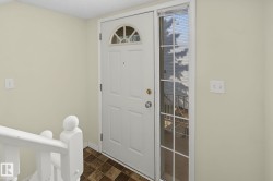 Entryway featuring a paneled door with an arched window, a full-length side window, a white painted railing, and patterned floor tile - 