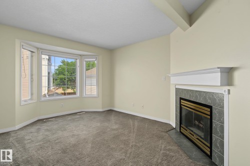 Light-filled interior featuring a bay window, wall-to-wall carpeting, a fireplace with a slate-look tile surround and white mantel, and neutral wall paint - 4259 29 Avenue, Edmonton, AB 