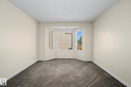 Recessed bay window with multiple panes, neutral wall paint, textured ceiling, and dark grey carpet flooring - 4259 29 Avenue, Edmonton, AB 