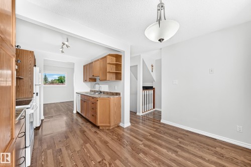 Kitchen area featuring wood-finish flooring, light wood cabinetry, stone-look countertops, and white appliances - 1102 Millbourne Road E, Edmonton, AB 