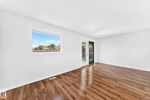 Spacious room featuring wood-finish flooring, a large window with horizontal blinds, and a glass-paned door - 1102 Millbourne Road E, Edmonton, AB 