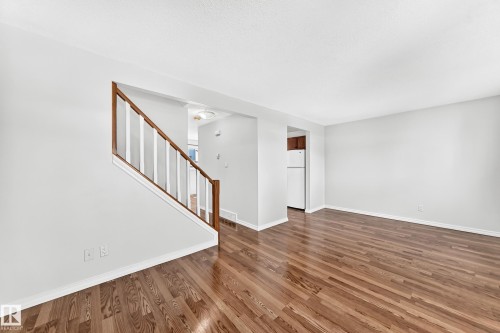 Spacious interior featuring wood-finish flooring, light gray wall paint, white trim, and a staircase with wood handrails and white balusters - 1102 Millbourne Road E, Edmonton, AB 