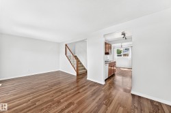 Spacious interior featuring wood-finish flooring, white baseboards, and a staircase with wooden handrails - 