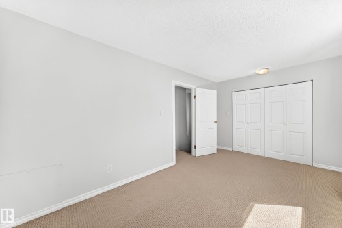 Bedroom featuring light neutral wall paint, white baseboards, a textured ceiling, flush-mount lighting, and beige carpeting - 1102 Millbourne Road E, Edmonton, AB 