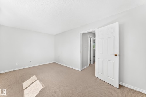 Spacious room with light neutral wall paint and carpeting, featuring a textured ceiling and white trim - 1102 Millbourne Road E, Edmonton, AB 