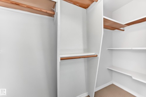 Walk-in closet featuring white built-in shelving, wood-finish hanging rods, and light-toned carpeting - 1102 Millbourne Road E, Edmonton, AB 