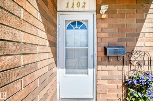 Brick exterior featuring a white entry door with an arched window, a wall-mounted mailbox, and an exterior light fixture - 1102 Millbourne Road E, Edmonton, AB 