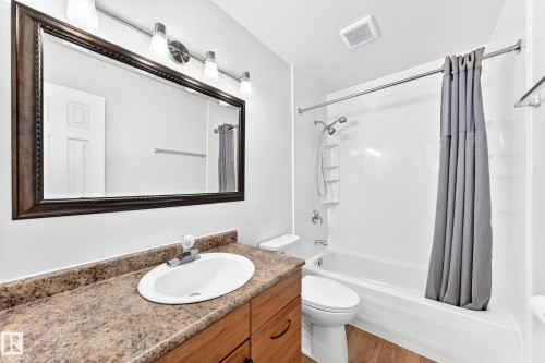Full bathroom featuring a wood-finish vanity with a built-in sink, a spacious framed mirror, and a white tub/shower combination - 1102 Millbourne Road E, Edmonton, AB 