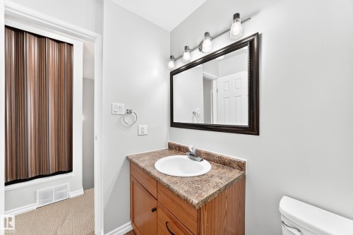 Vanity featuring a wood-finish cabinet, integrated sink, and stone-look countertop - 1102 Millbourne Road E, Edmonton, AB 