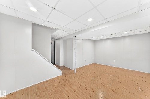 Open-concept finished basement with wood-finish flooring, white paneling, drop ceiling, and recessed lighting - 1102 Millbourne Road E, Edmonton, AB 
