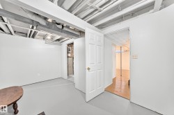 Unfinished basement space featuring exposed ceiling joists and ductwork, painted white walls, and a light gray finished concrete floor - 