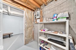 Unfinished basement area featuring exposed wooden joists, concrete walls, and a utility panel - 