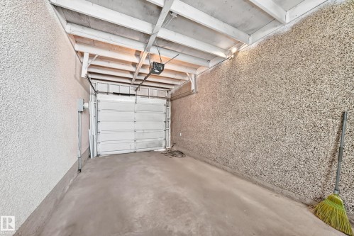 Single-bay garage featuring a concrete floor, an automatic garage door opener, and exposed ceiling joists - 1102 Millbourne Road E, Edmonton, AB 